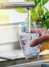 a person filling a glass with water from a kitchen faucet