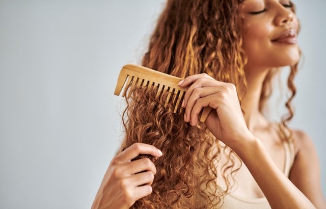 Woman brushing her curly hair with a wooden comb during her self care routine