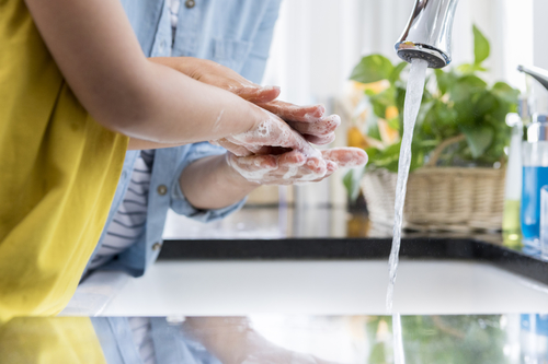 Child in yellow shirt washing hands with adult at kitchen sink