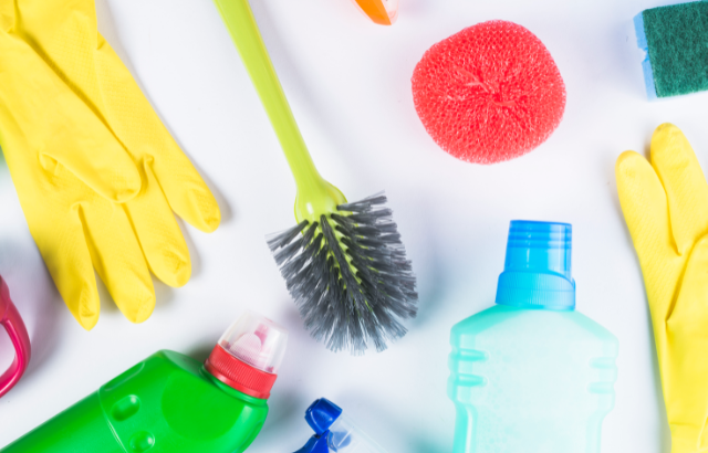 Cleaning supplies including rubber gloves, a scrub brush, and sponges laid out on a light colored background