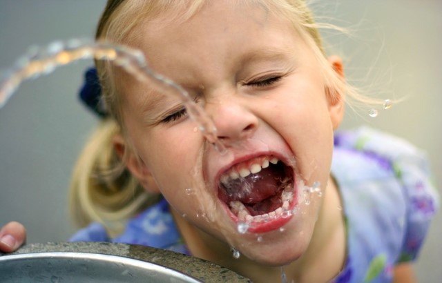 young girl drinking water from a water fountain